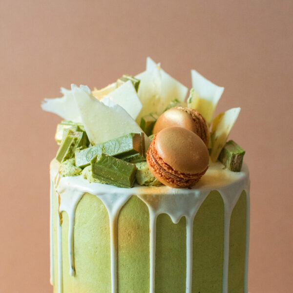 Close up of a matcha cake with white chocolate drip and macarons and green tea kitkats
