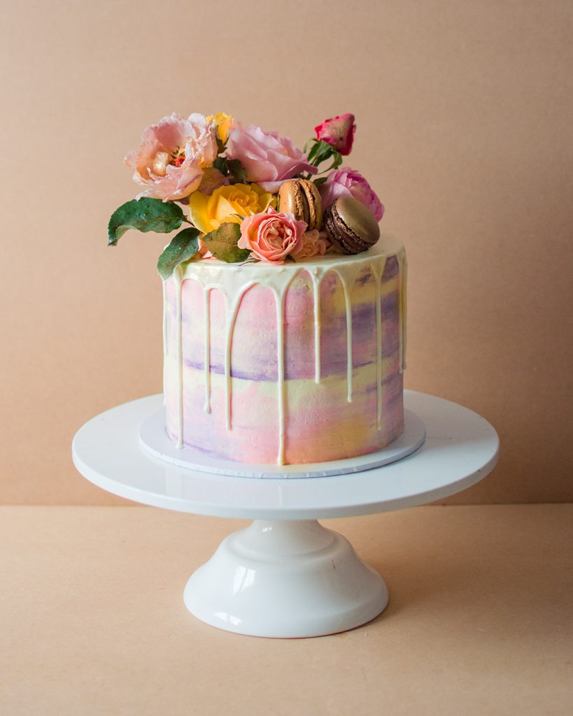 A small watercolour fairy birthday cake with pink and purple design and flowers on top