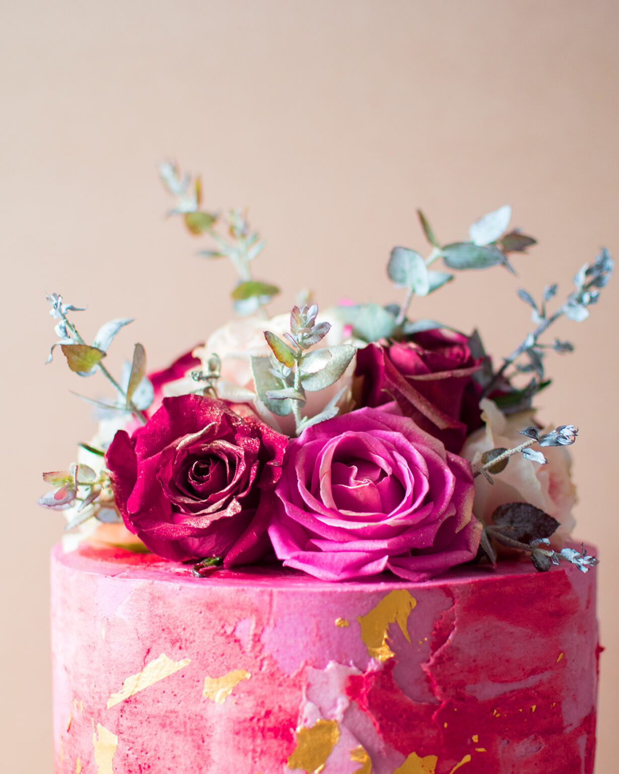 Close up of a pink cake with gold flakes and vintage flowers