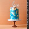 Tall birthday cake with blue shades on the sides and white chocolate drip and macarons on top