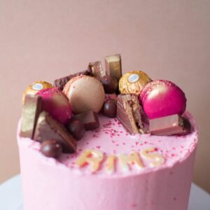 a close up image of a pink cake with various chocolates on top