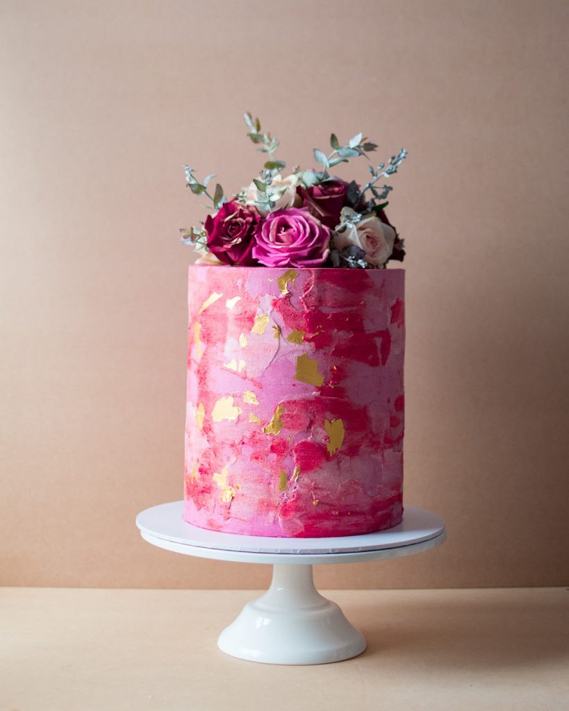 Single tier red cake with gold flakes and red and white flowers