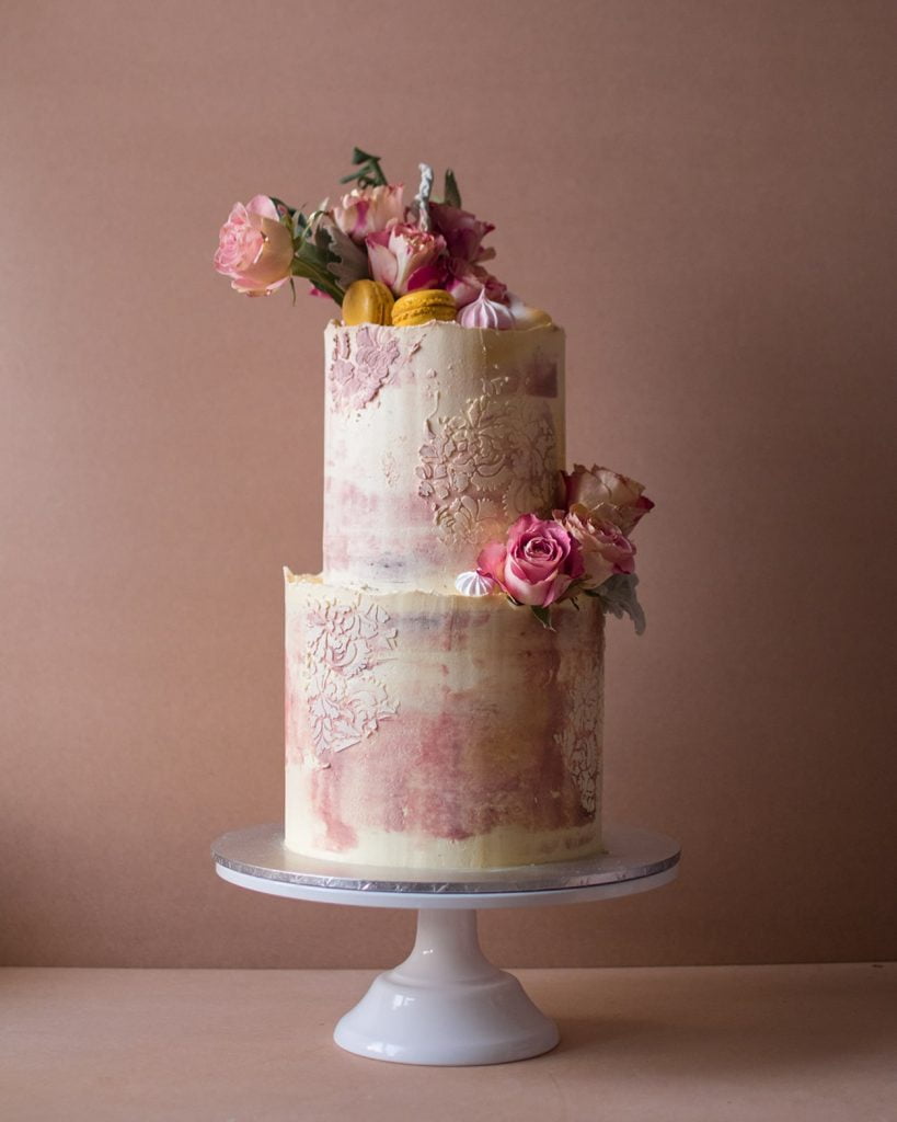 Two tier faded pink cake with pink and red flowers with macaroons