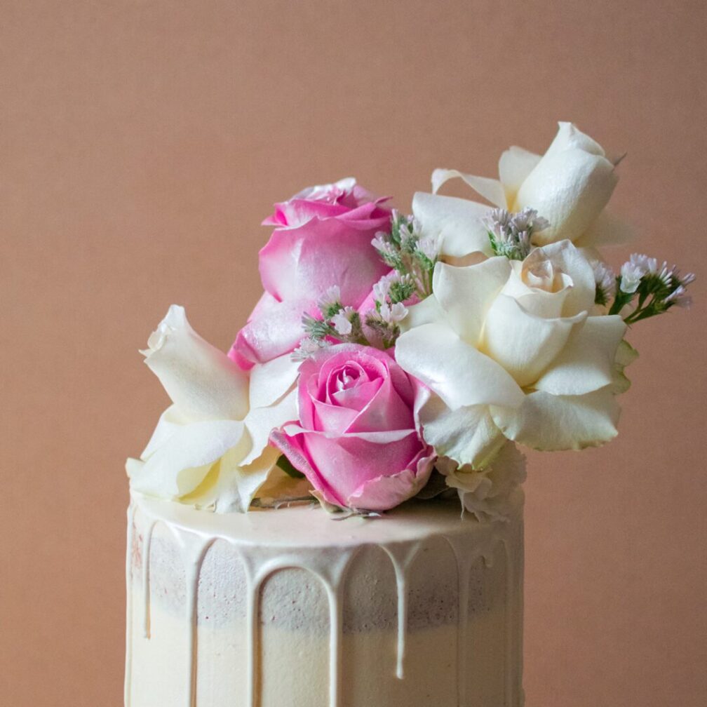 Close up of a white chocolate drip wedding cake with white and rose flowers